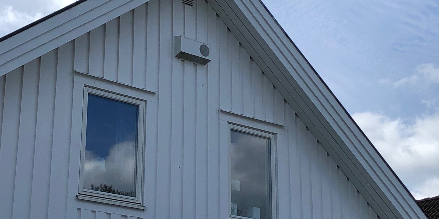 Diskret ytterväggshuv på vit träfasad