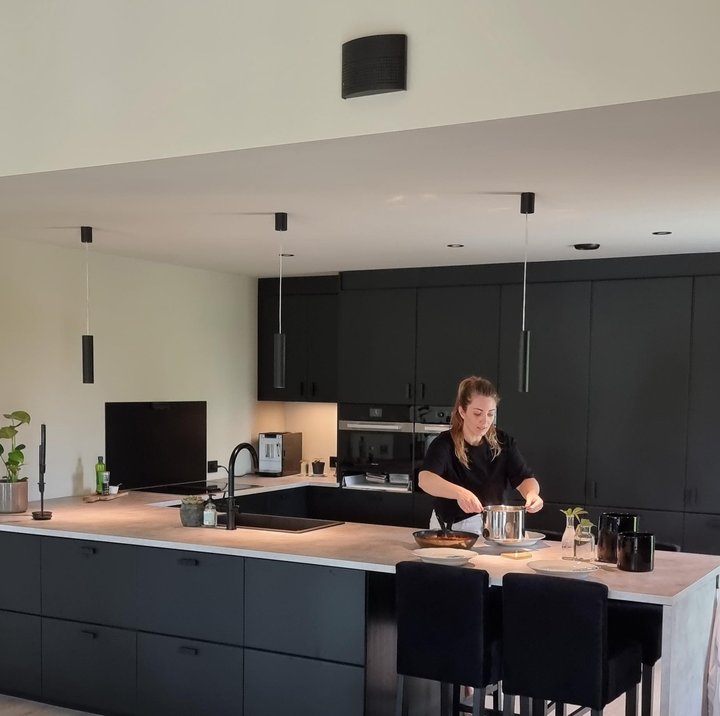 Moderne kjøkken med kjøkkenøy, integrerte skap og person som lager mat i åpen bolig.