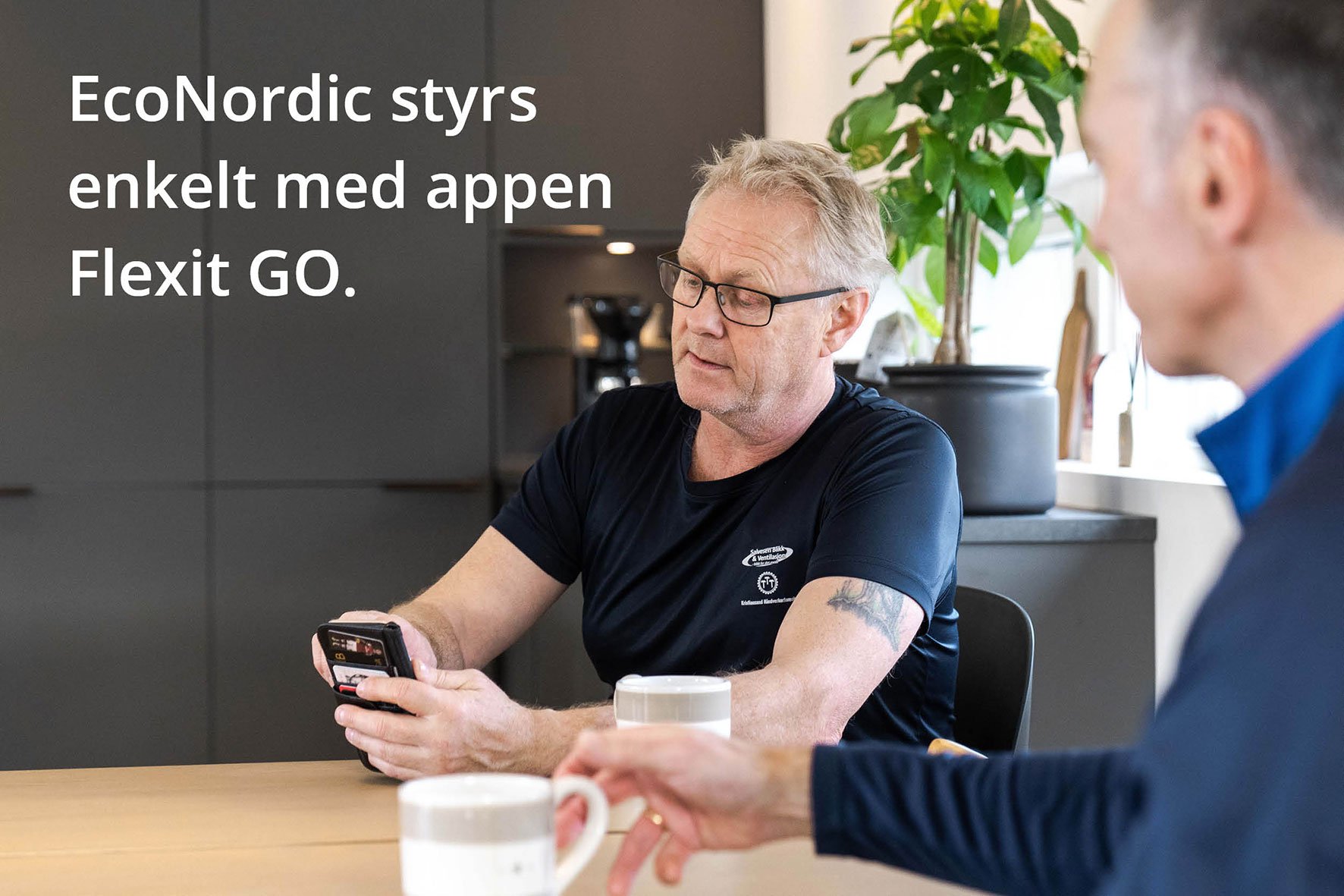 Man som styr Klimatvärmepump EcoNordic via Flexit GO-appen på mobilen vid köksbordet.