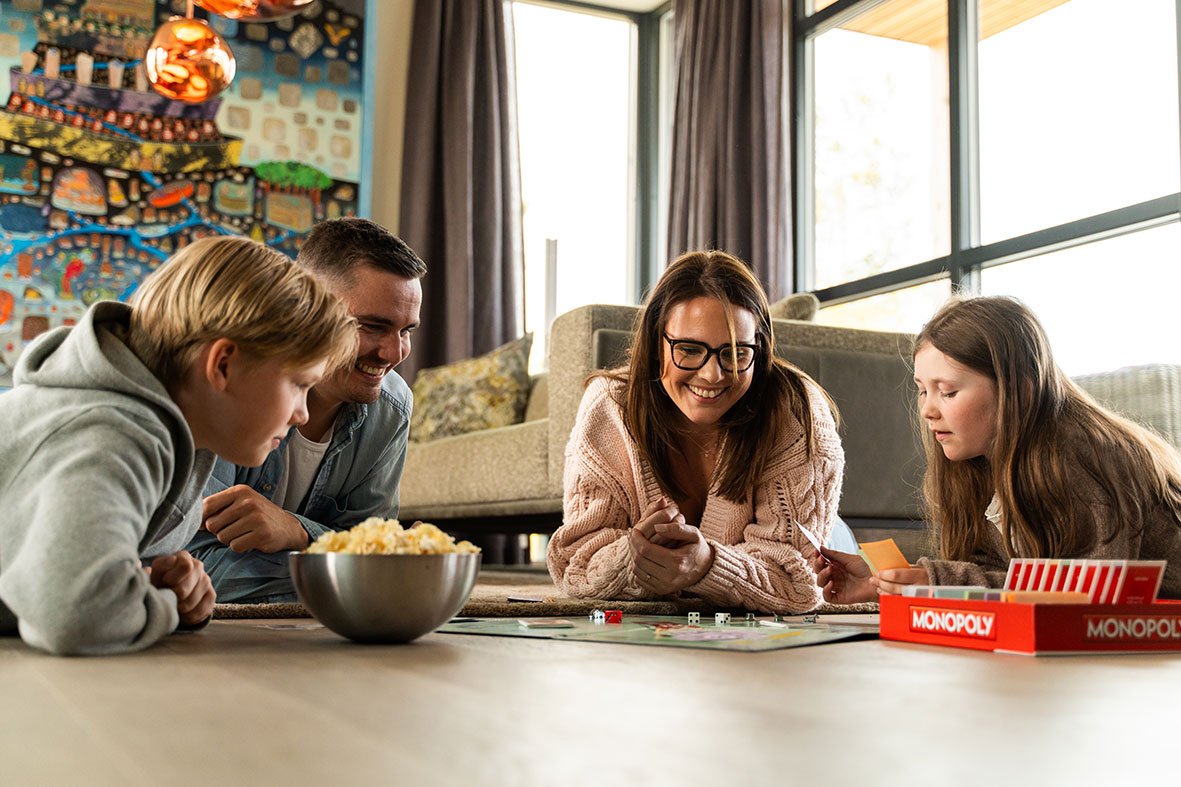 Familie som spiller brettspill i stuen i et lyst og komfortabelt innemiljø.