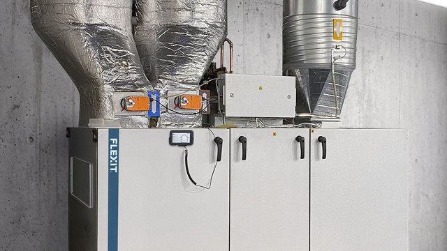 The image shows a ProNordic air handling unit installed in a technical room, with insulated ducts for supply and extract air. The solution is suited for larger residential buildings or commercial properties requiring reliable balanced ventilation.