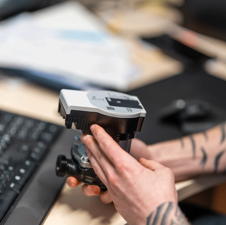 Hånd justerer måleinstrument på et skrivebord, brukt til teknisk arbeid.