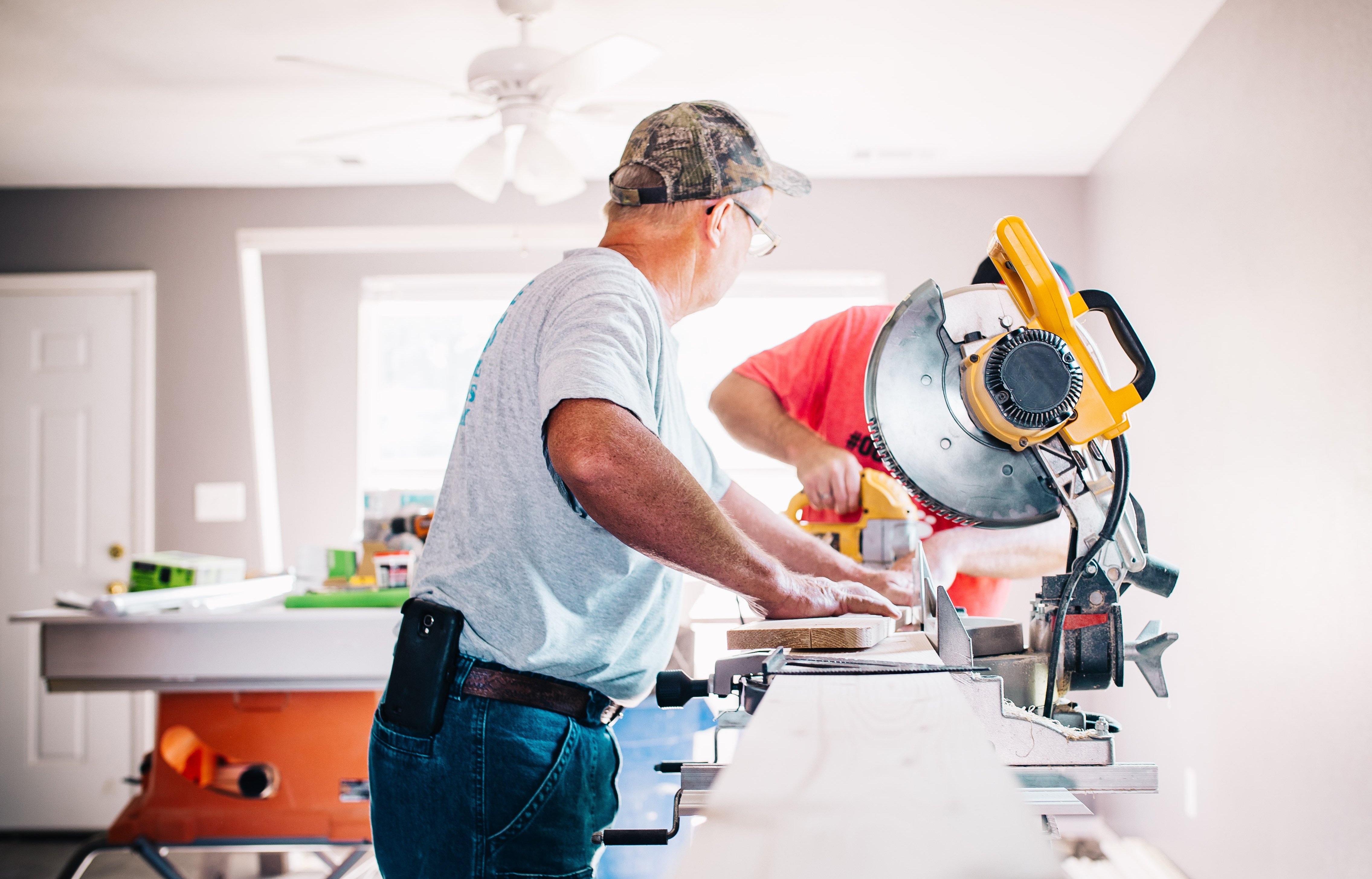 Personer pusser opp innendørs med sag og verktøy i boligrom under ombygging.