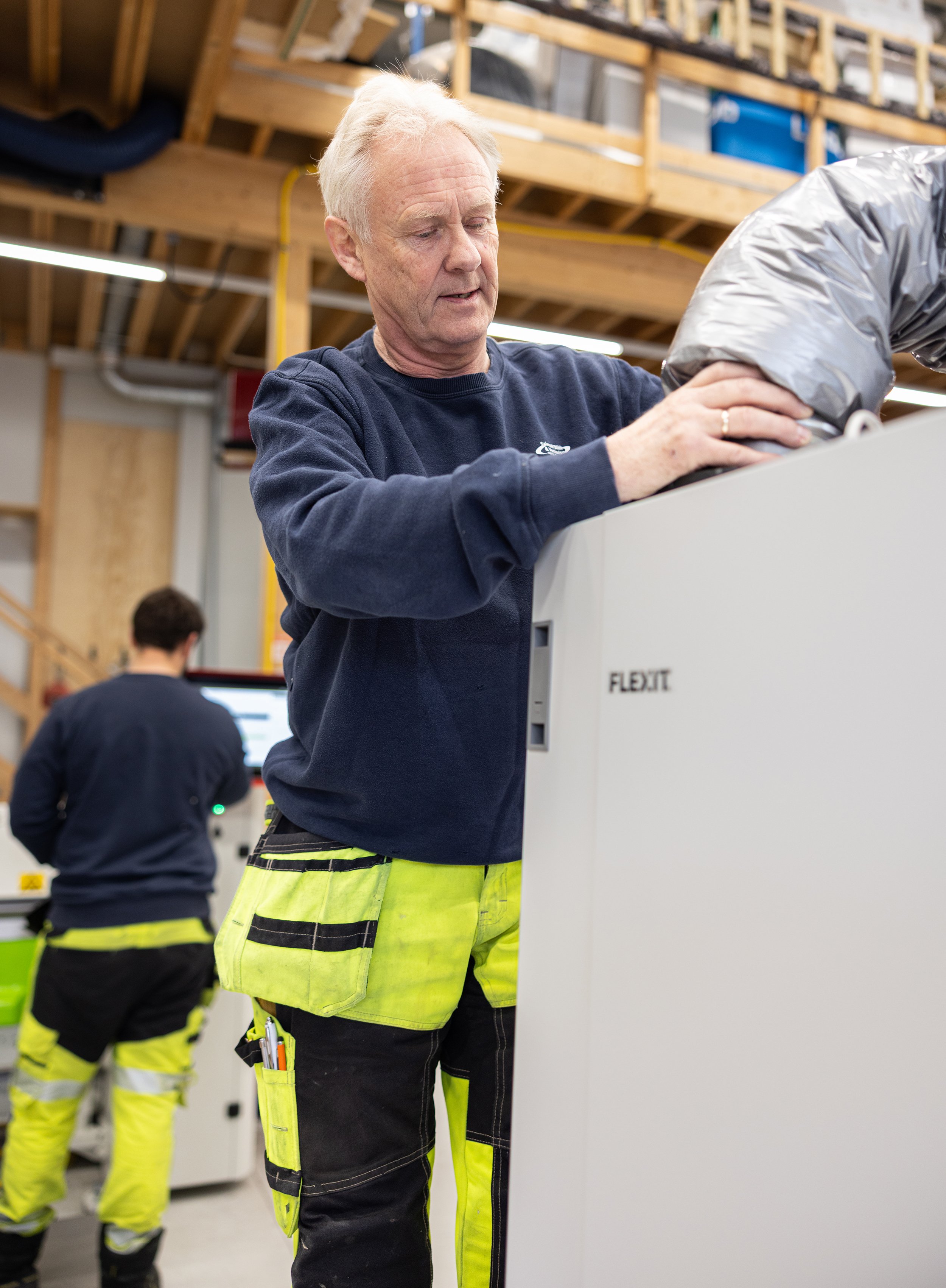 Representant fra Salvesen Blikk og Ventilasjon monterer et Flexit ventilasjonsaggregat i verksted.